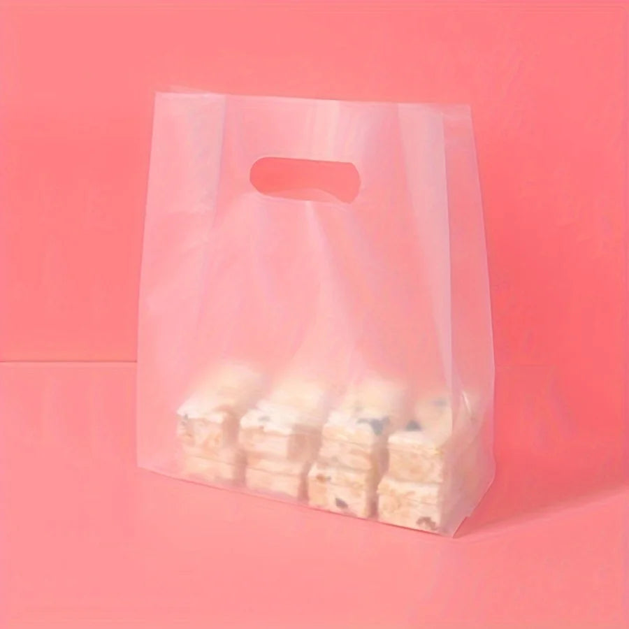 A clear plastic gift bag with a handle is filled with small white and blue layered treats on a pink background.