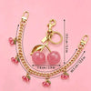 Gold chain necklace featuring pink glass cherry charms and a pendant on a pink background.