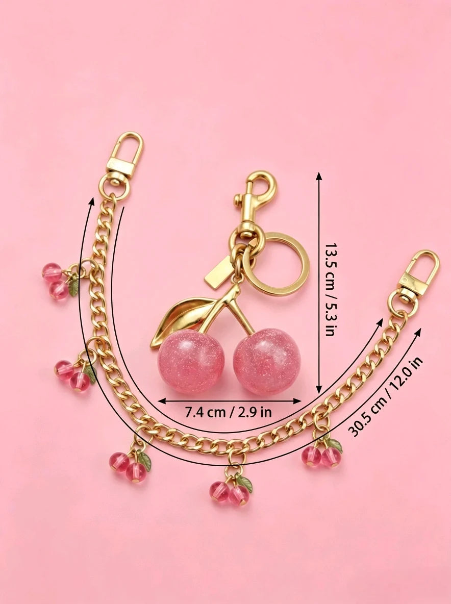 Gold chain necklace featuring pink glass cherry charms and a pendant on a pink background.