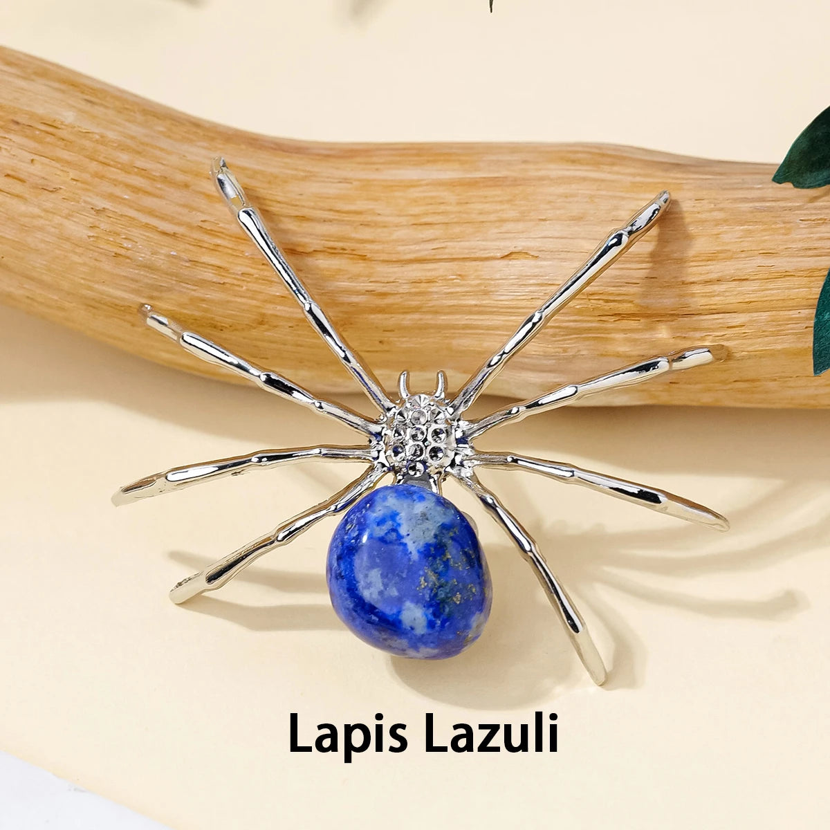 A silver crystal spider figurine with blue lapis lazuli stone resting on a wooden surface.