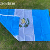 A rectangular flag of Guatemala with blue and white vertical stripes displayed outdoors on green grass.