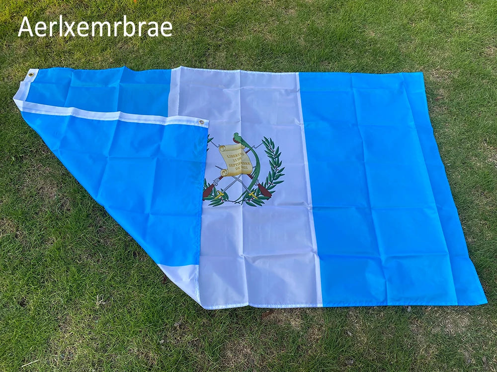 A rectangular flag of Guatemala with blue and white vertical stripes displayed outdoors on green grass.