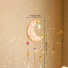 A golden crescent moon dreamcatcher with hanging crystal beads and a rainbow prism, suspended from a wooden branch.