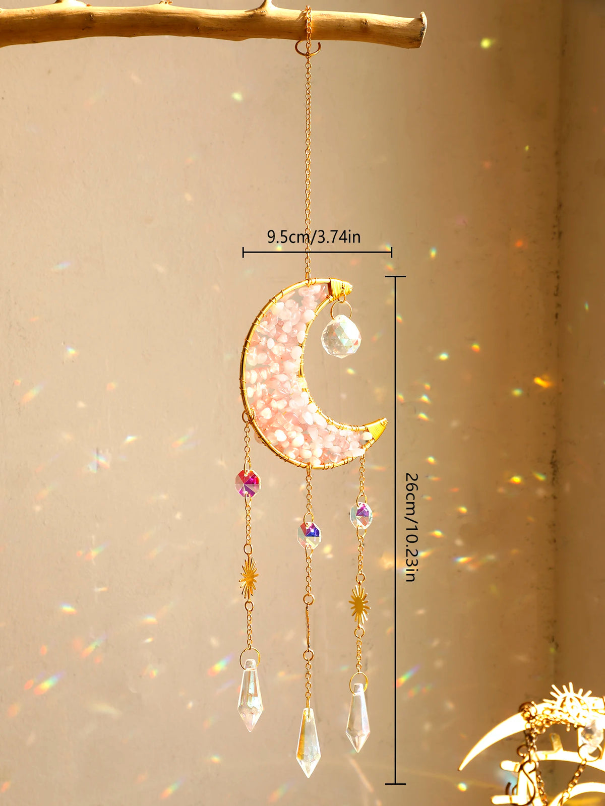 A golden crescent moon dreamcatcher with hanging crystal beads and a rainbow prism, suspended from a wooden branch.