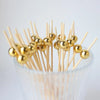 Gold accent bamboo cocktail skewers with spherical balls arranged in a clear glass