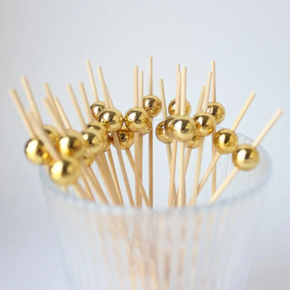 Gold accent bamboo cocktail skewers with spherical balls arranged in a clear glass