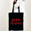 A black tote bag featuring the text Merry Christmas in pink script, held by a person.