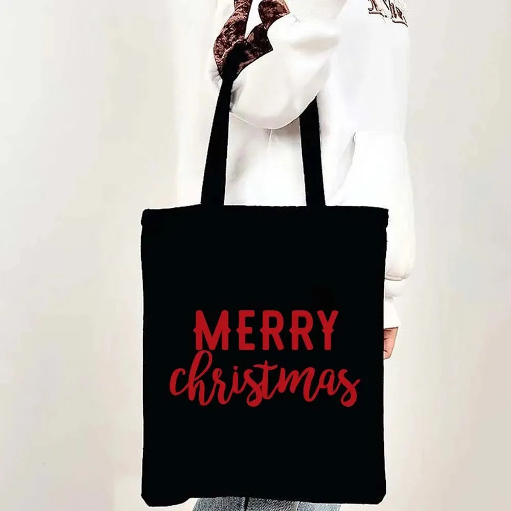 A black tote bag featuring the text Merry Christmas in pink script, held by a person.