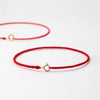 A handmade red string bracelet with a gold plated clasp lying on a white surface.