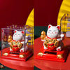 A red solar-powered figurine of a white cat with gold accents, sitting on a red base.