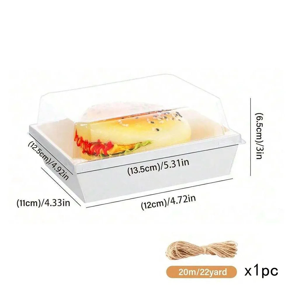 A white rectangular box with a clear lid holds a sliced pastry or sandwich, shown next to a measuring scale.