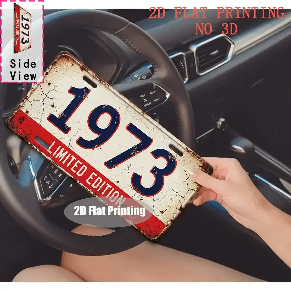 A distressed vintage metal tin sign shaped like a license plate with the year 1973 is held in a hand.