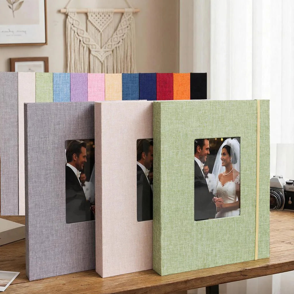 A row of linen photo albums in various pastel and dark colors displayed on a wooden table.