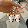 A pair of handmade crochet cow keychains with black and white patterns hanging from a gold-colored chain.