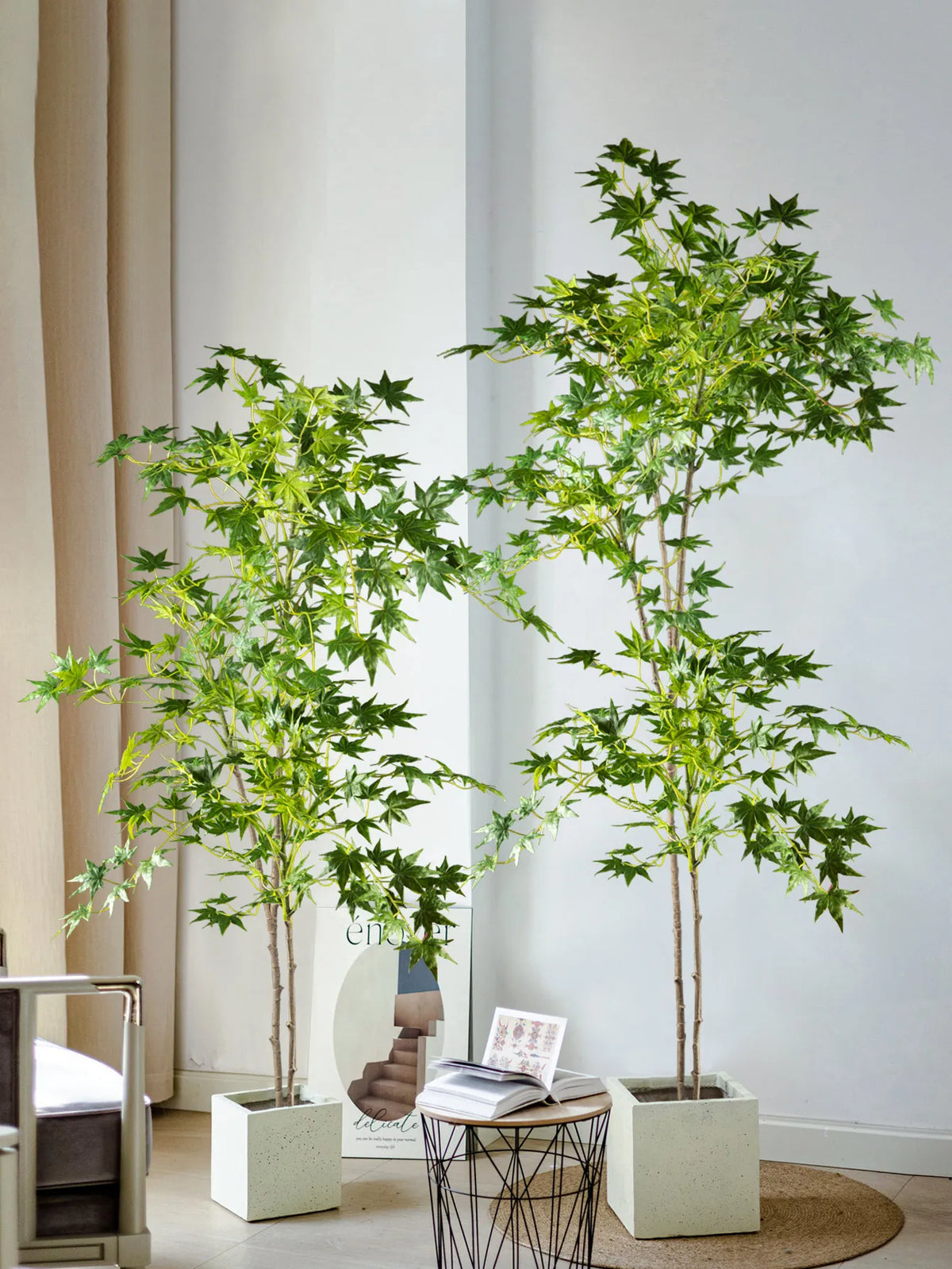 A tall artificial maple tree with silk green leaves displayed in a white planter against a light wall.