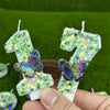 A hand holds a green sequin butterfly number candle for birthday cakes against a green background.