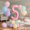 Un amas de ballons en feuille roses et vert clair formant le chiffre cinq sur une table blanche.