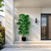 A large artificial palm tree in a black pot displayed on a light-colored step outside a modern building.