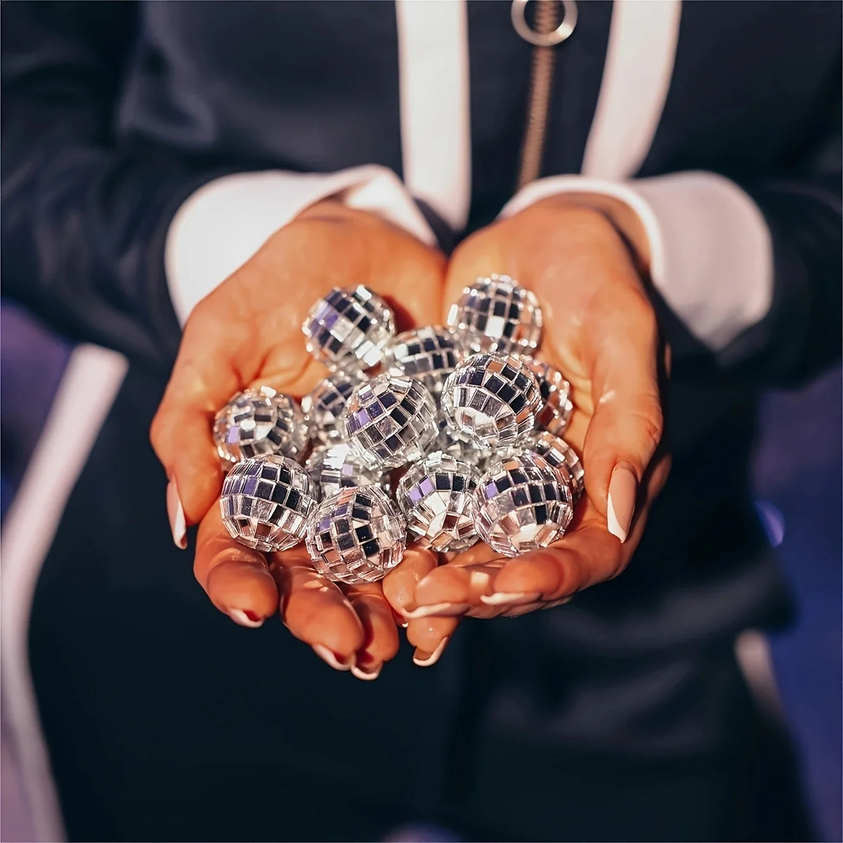 A person's hands holding a cluster of small, reflective disco mirror balls for party decor.