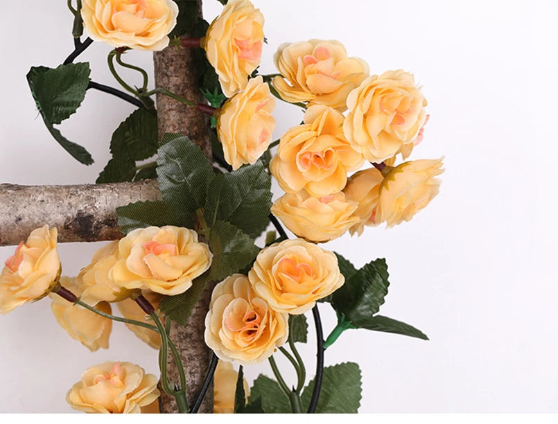 A silk rose vine garland featuring yellow and peach colored roses attached to a wooden cross branch.