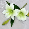 White artificial lilies with green buds and leaves displayed on a light fabric.