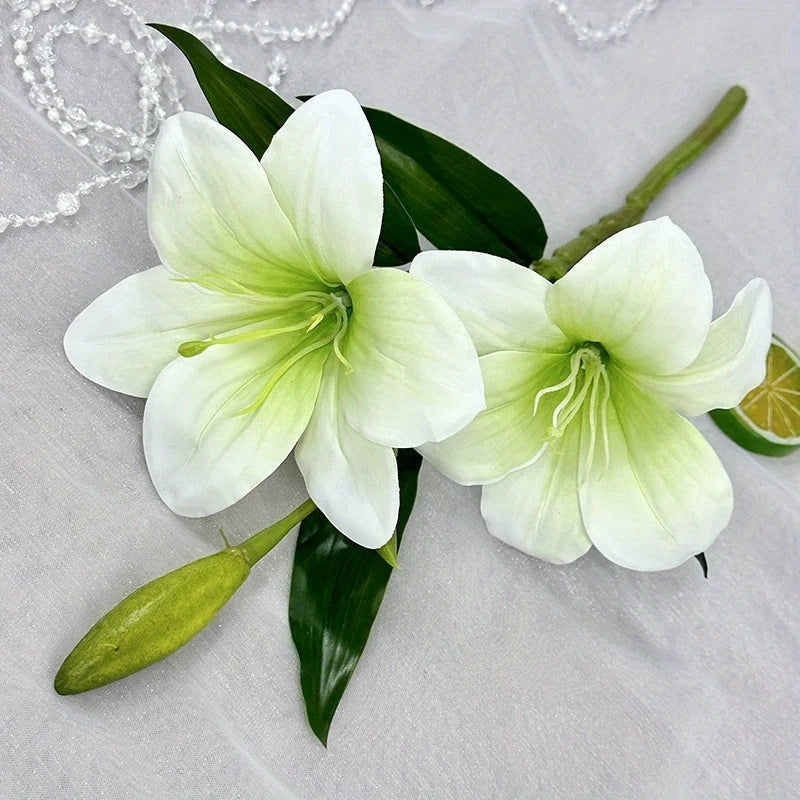 White artificial lilies with green buds and leaves displayed on a light fabric.