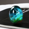 A clear resin ornament shaped like an elk deer with antlers, set in a vibrant blue and green landscape.