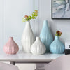 A collection of elegant ceramic flower vases in pink and light blue tones displayed on a white table.