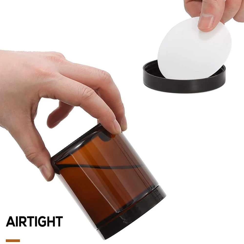A hand is shown placing a white disc into an amber glass candle jar with a black metal lid.