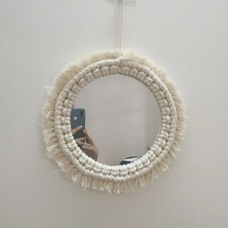 Miroir rond encadré par une corde macramé crème épaisse et des franges, accroché à un mur blanc.