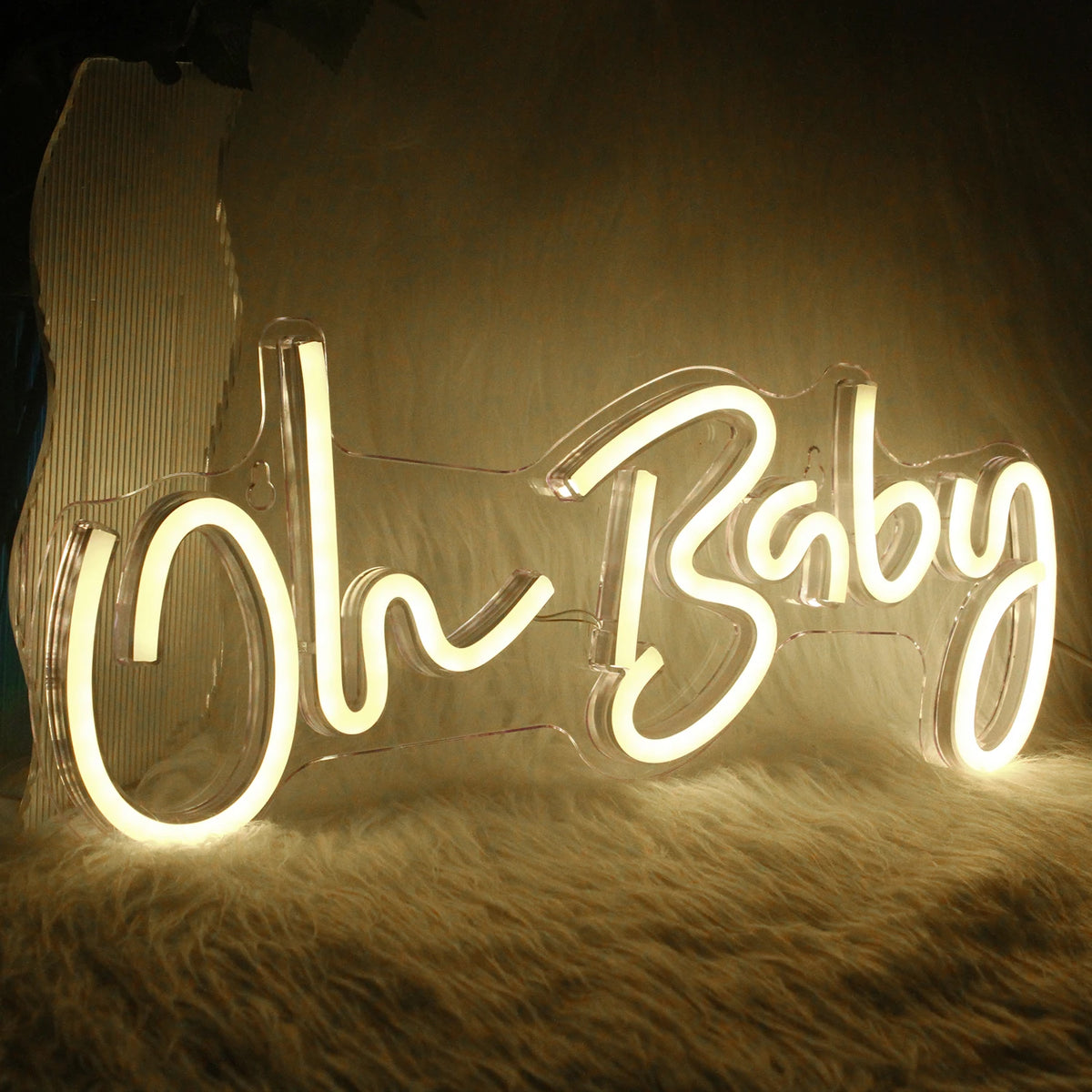 A glowing neon sign spelling out Oh Baby rests on a fluffy surface.