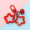 A red star-shaped charm pendant keychain with a metal clasp is displayed on a light pink and blue background.