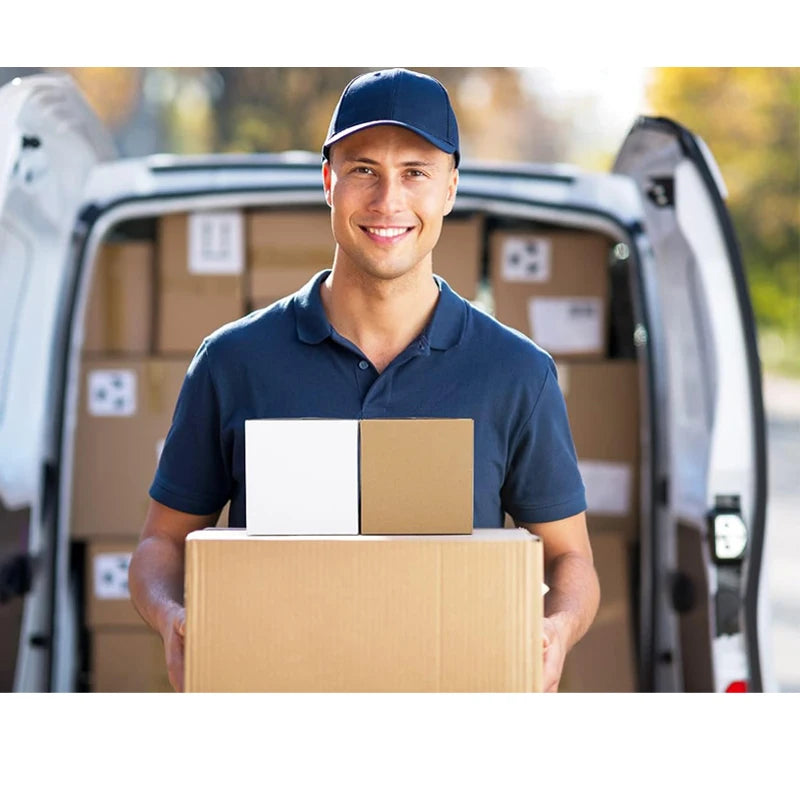 A smiling man in a blue shirt holds a cardboard box in front of a van full of stacked shipping boxes.