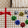A collection of holographic and glitter star gift bows in red, silver, gold, blue, and green scattered on brown patterned pap