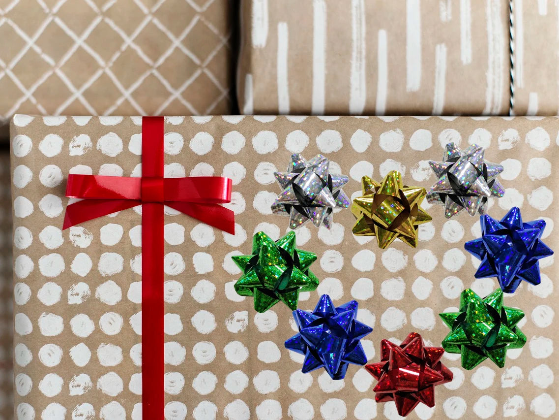 A collection of holographic and glitter star gift bows in red, silver, gold, blue, and green scattered on brown patterned pap
