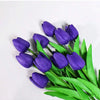 A bouquet of six deep purple artificial tulips with bright green leaves.