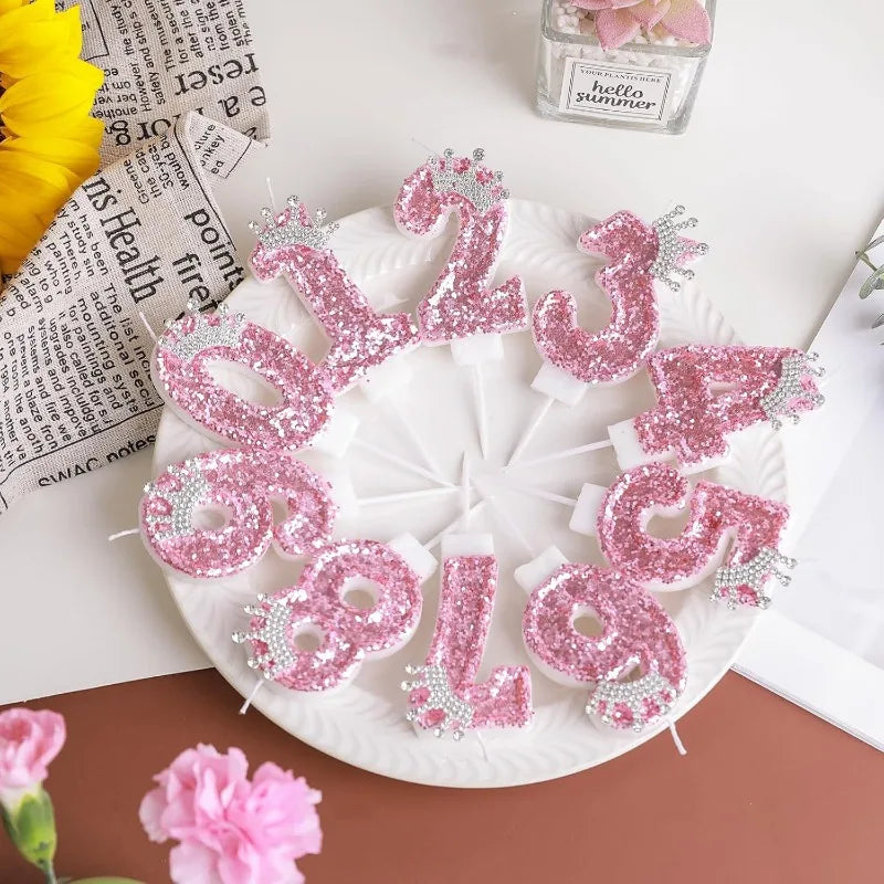 Pink sequin birthday number candles with crown toppers arranged on a white plate.