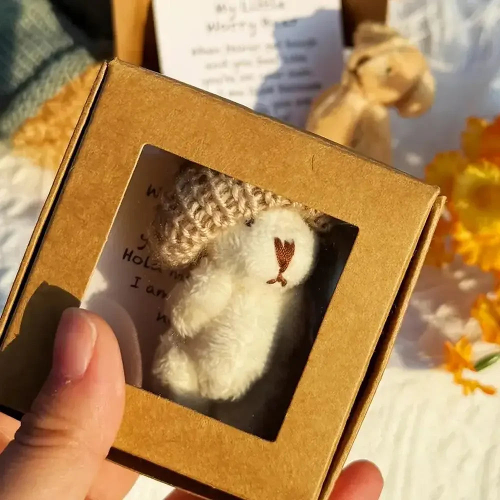 Una mano sostiene una pequeña caja de cartón con un peluche de oso blanco esponjoso y una tarjeta inspiradora.