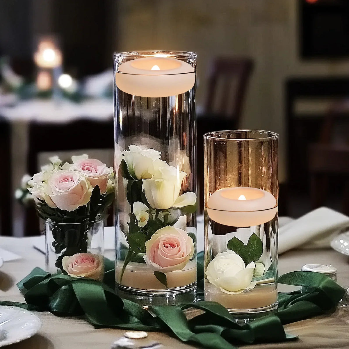 A glass vase holds several floating LED candles and roses on a table setting.