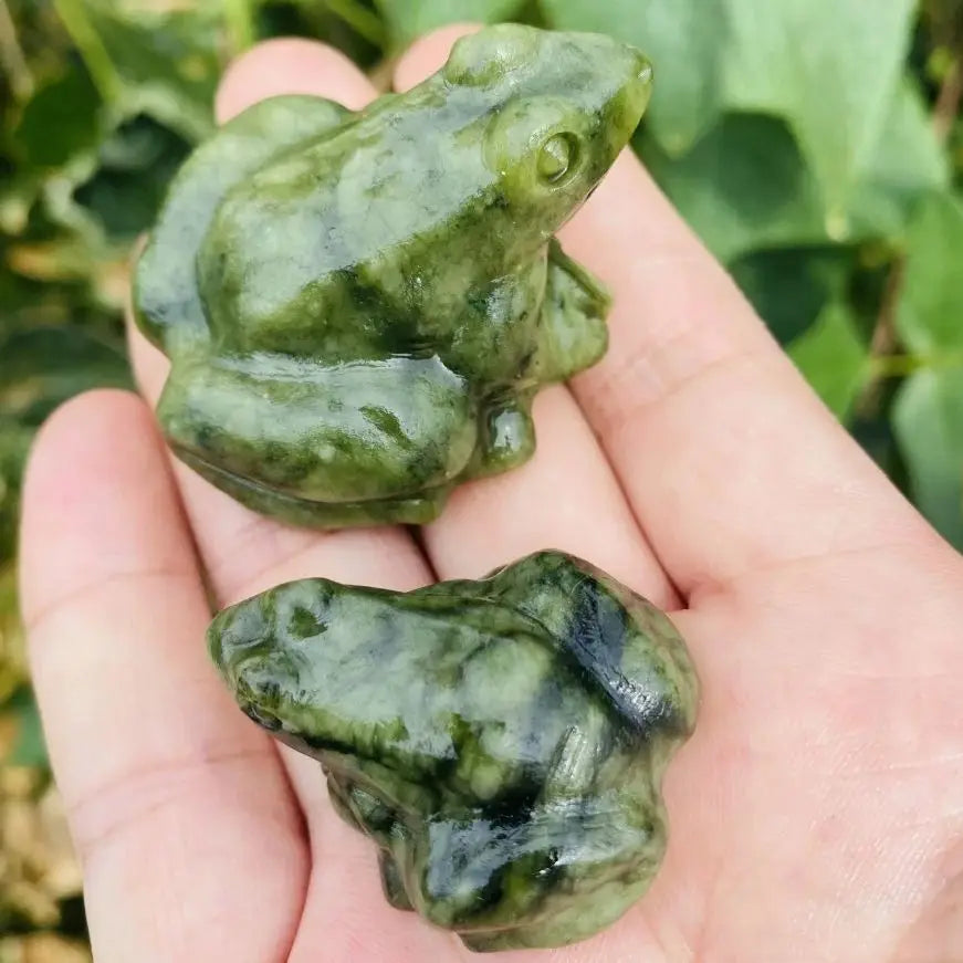 Une main tient une figurine miniature de grenouille de jade verte sur un fond vert flou.