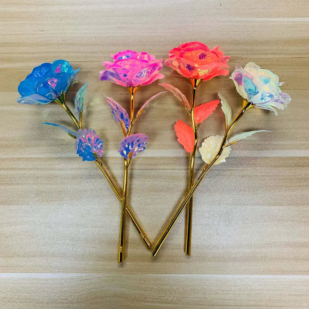 A bouquet of glowing gold foil roses in various shades of blue, pink, and orange on a light wooden surface.