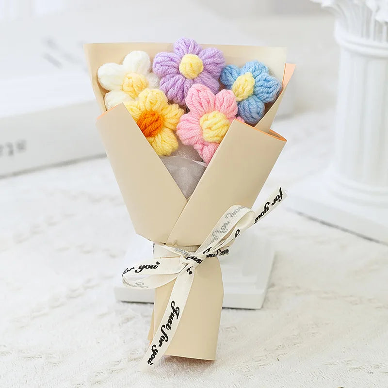 A bouquet of handmade crochet flowers in pastel colors like yellow, purple, and blue, presented in a light kraft paper wrappi