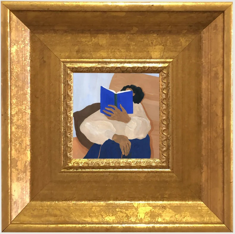 A painting of a person reading a blue book, framed in an elegant gold picture frame.