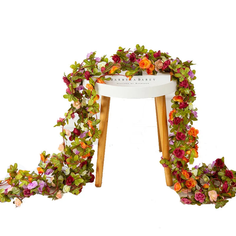 A silk rose garland featuring various colored roses and greenery draped over a white wooden arch.