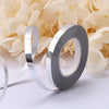 Roll of silver satin balloon ribbon lying on a white surface next to light yellow flowers