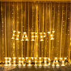 Golden curtain decorated with warm LED letter lights spelling HAPPY BIRTHDAY