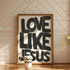 Framed black text saying Love Like Jesus on a canvas print displayed on a wooden floor.