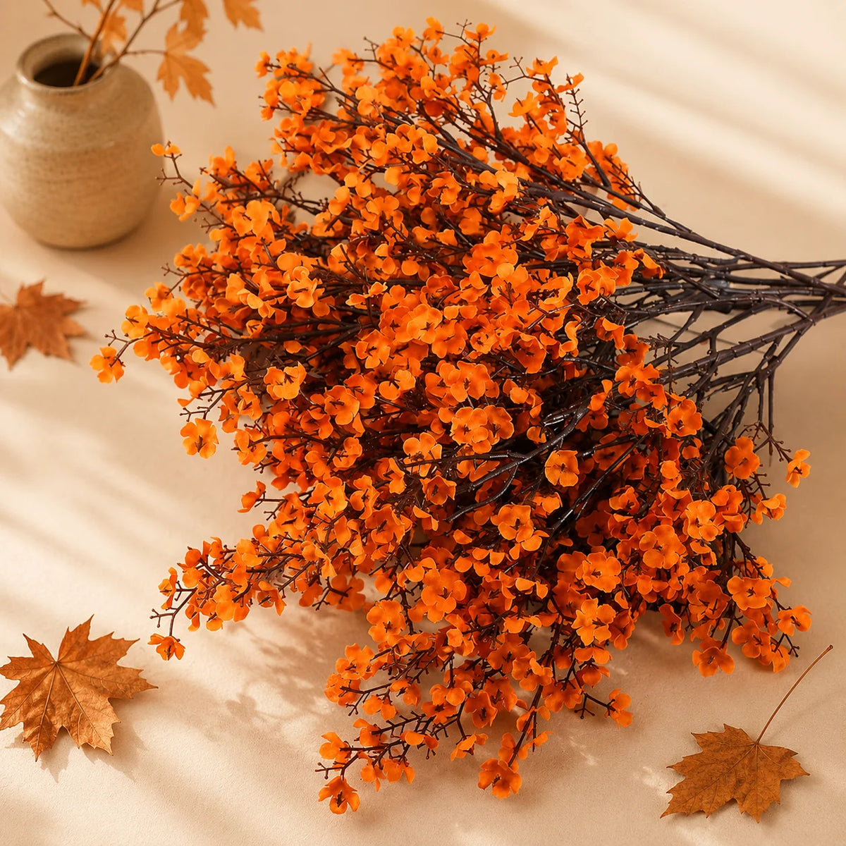 A bouquet of artificial orange baby's breath flowers with dark branches on a light background.