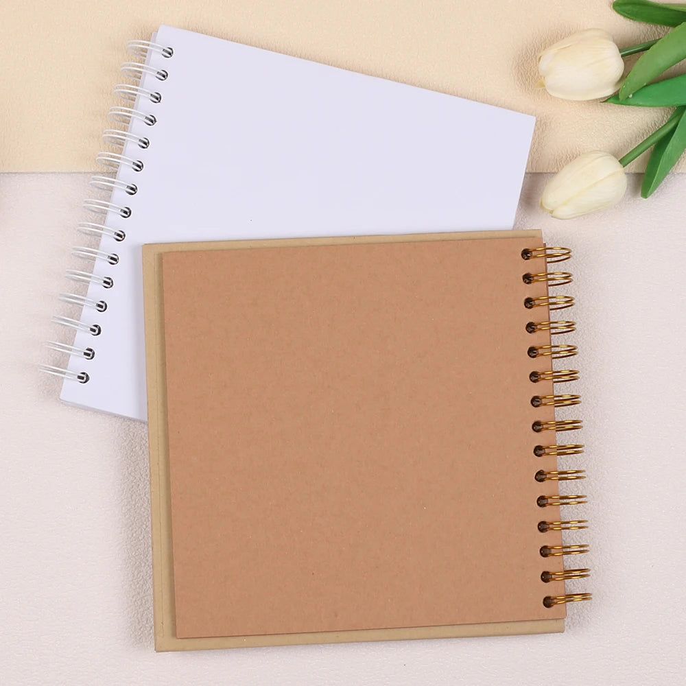 A brown spiral-bound kraft paper notebook lying next to a white spiral-bound notebook and a white tulip.