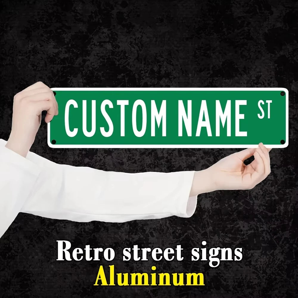 A hand holds up a green aluminum street sign with the text CUSTOM NAME ST